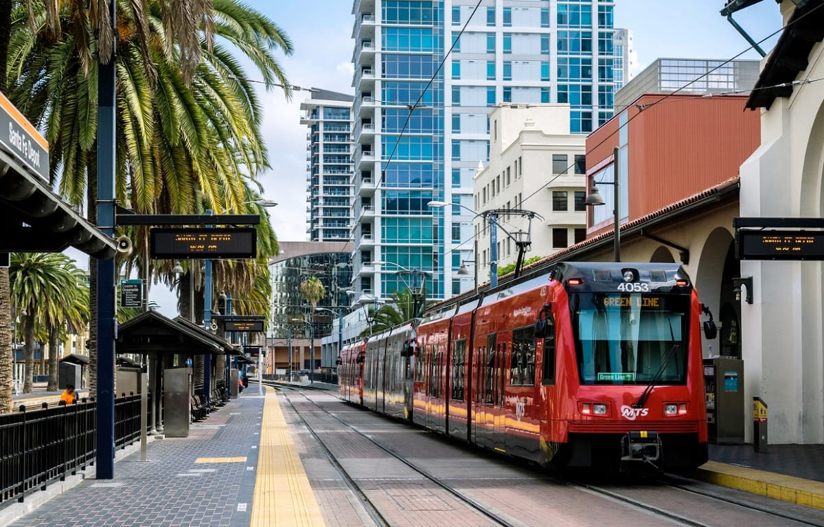 A light rail train framed by a palm tree and a high-rise apartment.