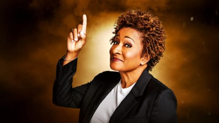 Wanda Sykes, smiling at the camera and pointing upwards