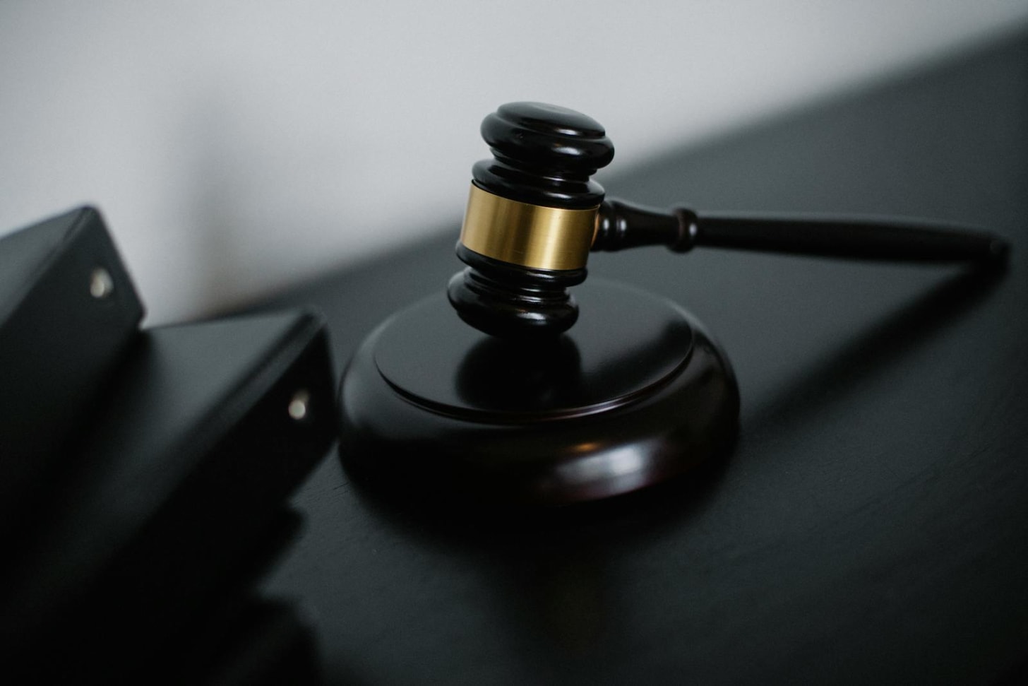 A wooden gavel resting on a law book beside a quiet courtroom bench