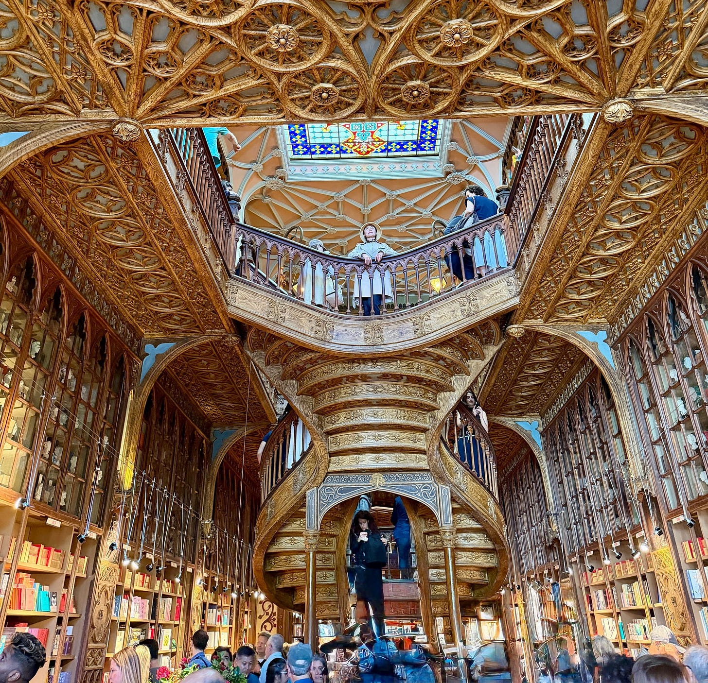 The ornate carved wooden staircase inside Livraria Lello bookshop in Porto, Portugal, with gilded Art Nouveau details, floor-to-ceiling bookshelves, and a stained glass ceiling