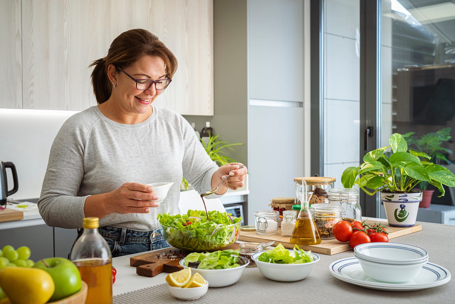 Smiling woman drizzles dressing over a fresh green salad.