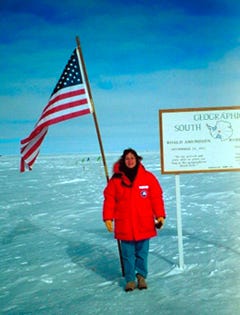 Person in red parka holds American flag at South Pole.