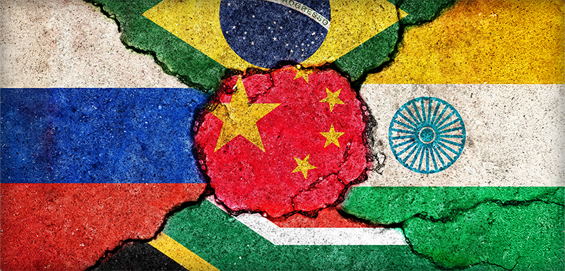 Cracked concrete painted with the BRICS nations’ flags — Brazil, Russia, India, China, and South Africa. China’s red flag with yellow stars is at the center, surrounded by the others, symbolizing tension, fragmentation, and geopolitical shifts among these emerging economies.