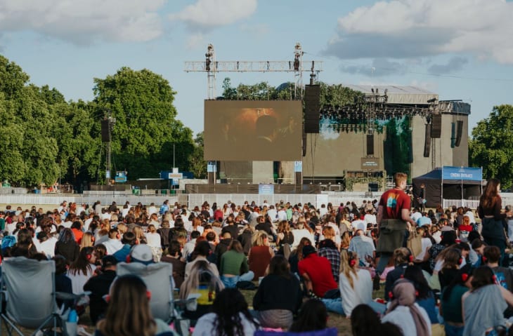 People sitting on grass watching a film on a large screen