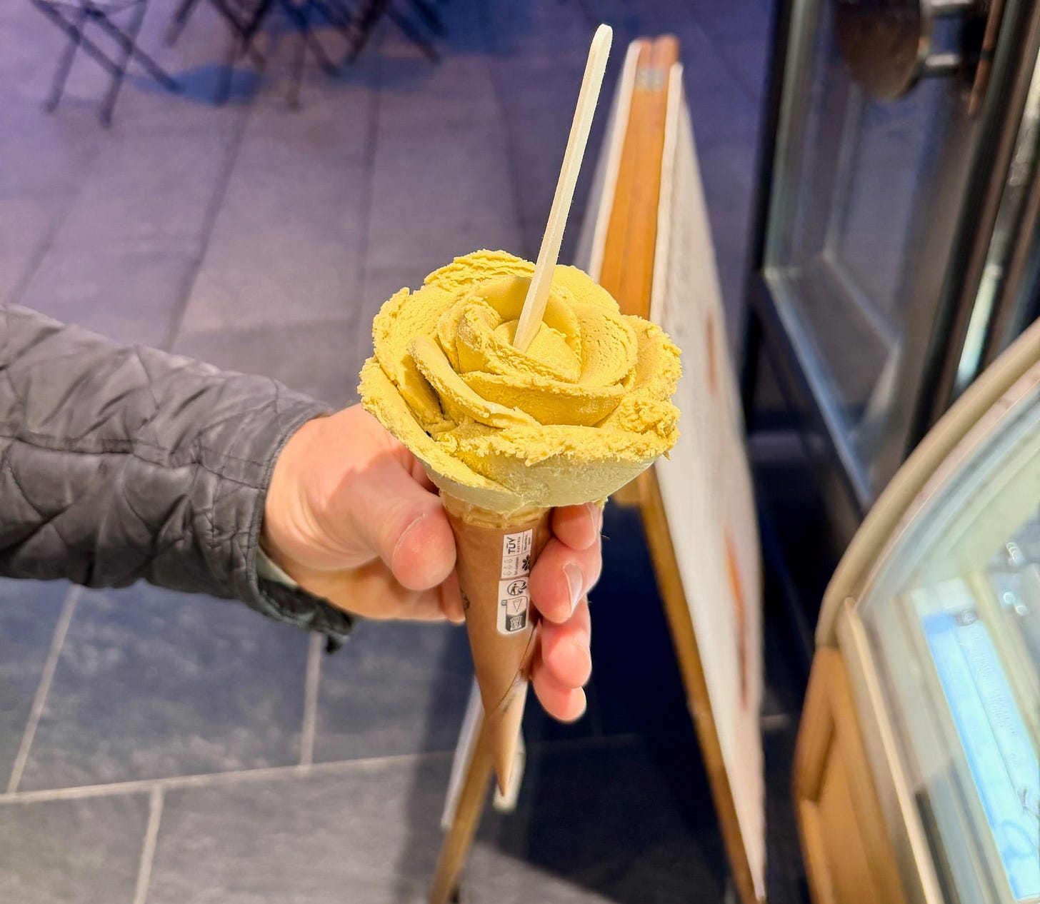 A rose-shaped gelato cone from Amorino in Porto, Portugal, sculpted in a pale golden yellow flavor and held up against a tiled floor background