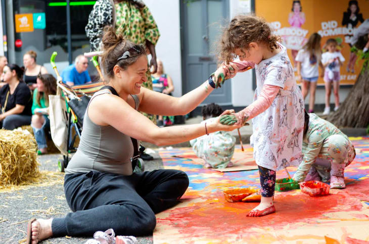 A woman helping a young girl paint with her feet