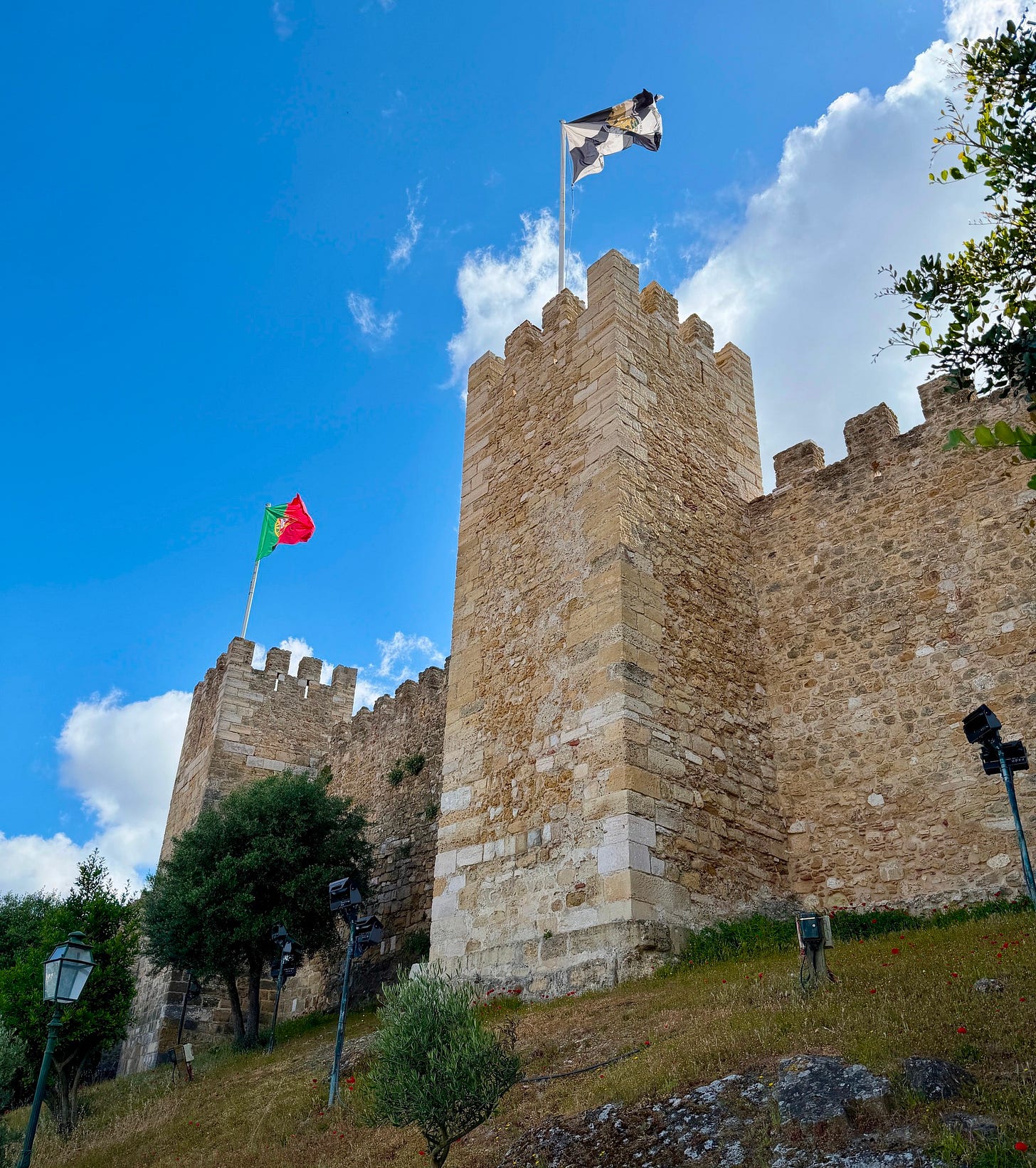 A stone watchtower at Castelo de São Jorge in Lisbon with the Portuguese flag flying against a clear blue sky, seen from the castle grounds