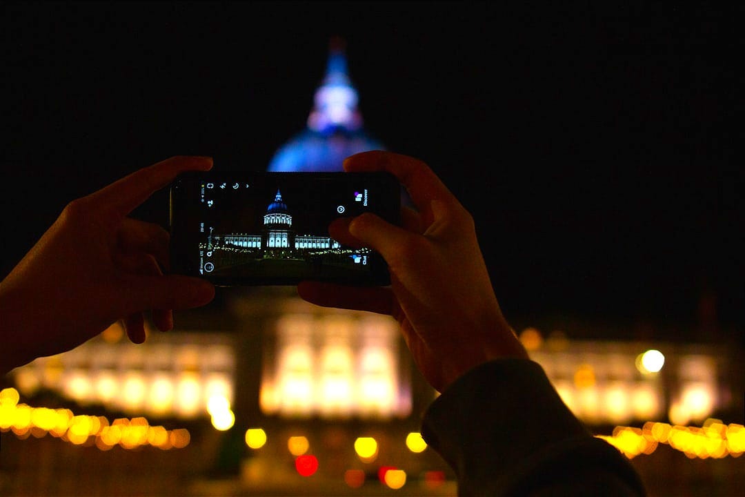 person holding black smartphone taking photo of city lights during night time