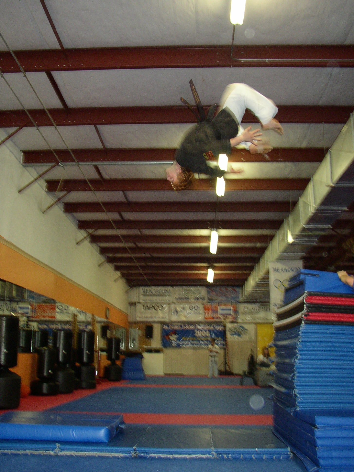 Martial artist performing aerial flip in training gym with mats