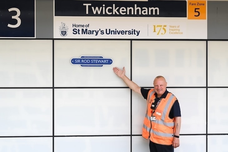 A man points out a plaque to Rod Stewart on a station wall