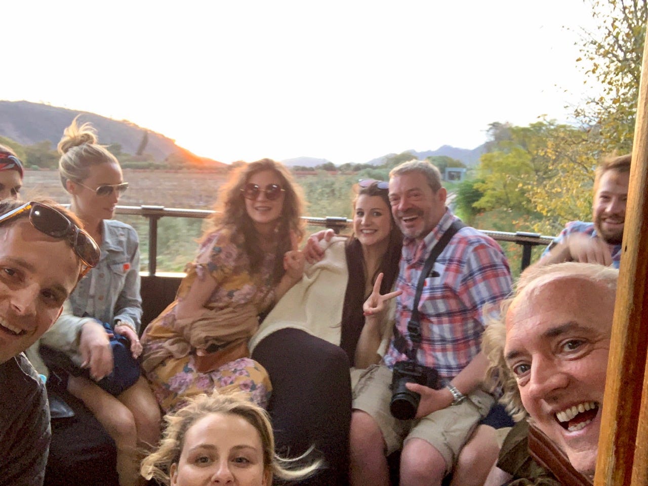 A large group of people crammed into a win tram at golden hour, vineyard-covered hills golden in the background, everyone smiling.