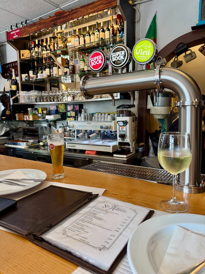The bar at Taberna Santo António in Porto, Portugal, with a glass of Superbock beer and Vinho Verde wine in the foreground and the restaurant menu visible on the counter