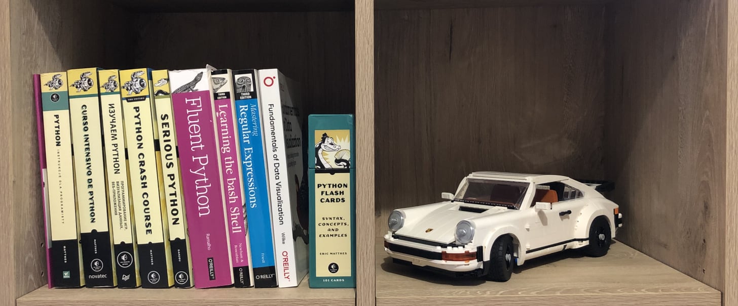Bookshelf with a number of programming books, a box of flash cards, and a LEGO car on it.
