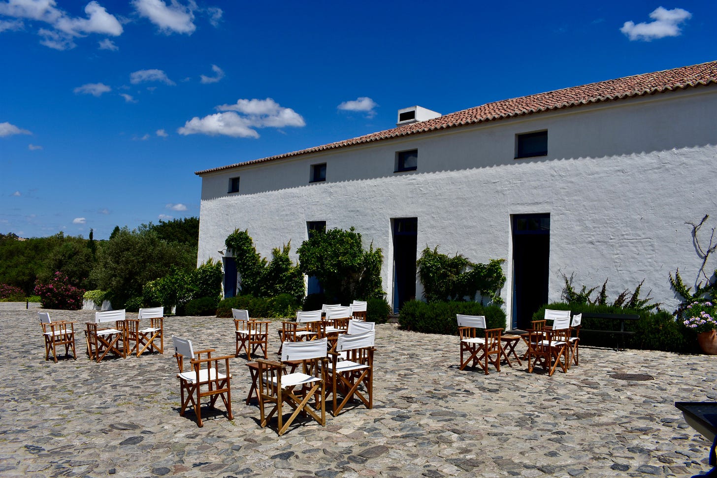 Wooden director's chairs with white canvas arranged on a cobblestone terrace, set against the whitewashed hotel building for cocktail hour