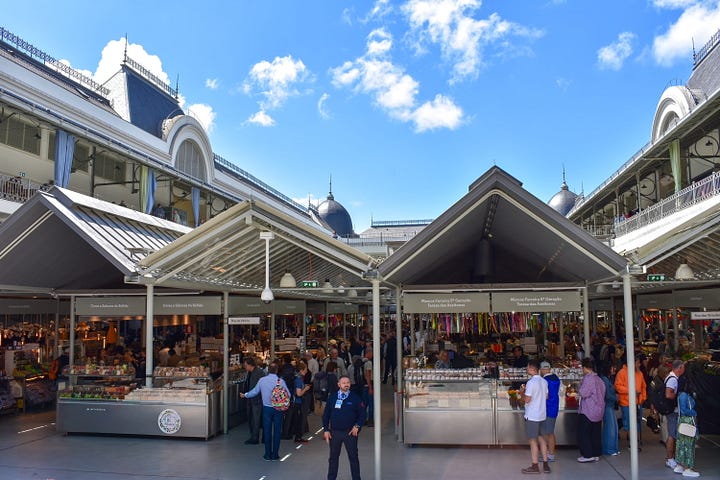 The interior of Mercado do Bolhão in Porto, Portugal, with market stalls, vendors, and shoppers under the renovated iron-and-glass market hall roof