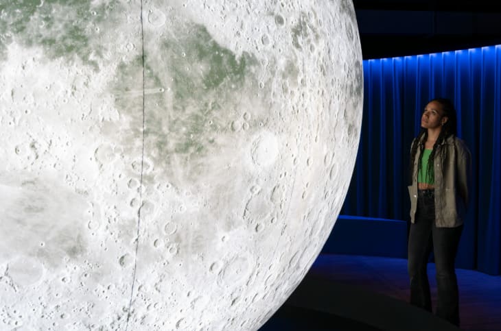 A woman standing beside a scale model of the Moon