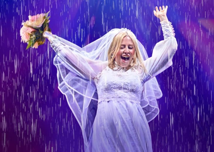 A woman on stage in a wedding dress in the rain