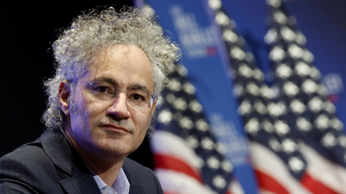 A photo of Palantir CEO Alex Karp with American flags in the background. 