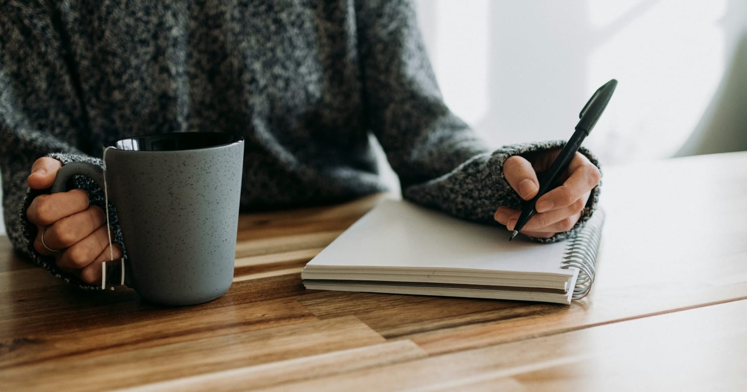 uma pessoa segurando uma caneta e escrevendo em um caderno