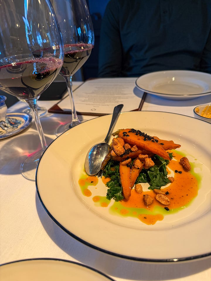 Roasted carrots with kale, toasted almonds, and herb oil alongside a glass of red wine at dinner — São Lourenço do Barrocal's restaurant cooking is rooted in Alentejan tradition