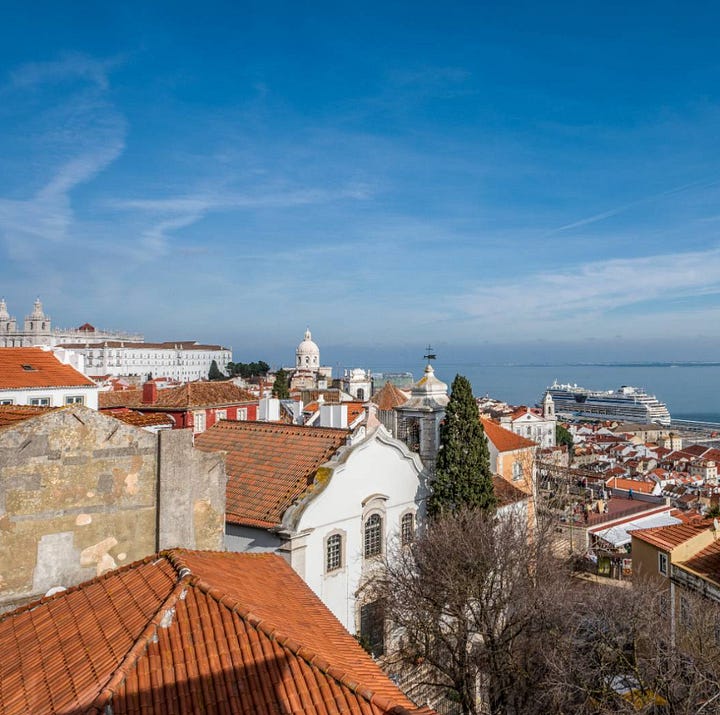 View over Alfama's red-tiled rooftops in Lisbon from above, with a white church bell tower.