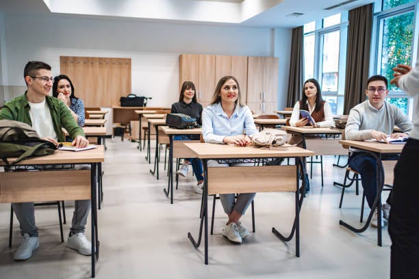 Students sitting in a classroom listening to their  teacher