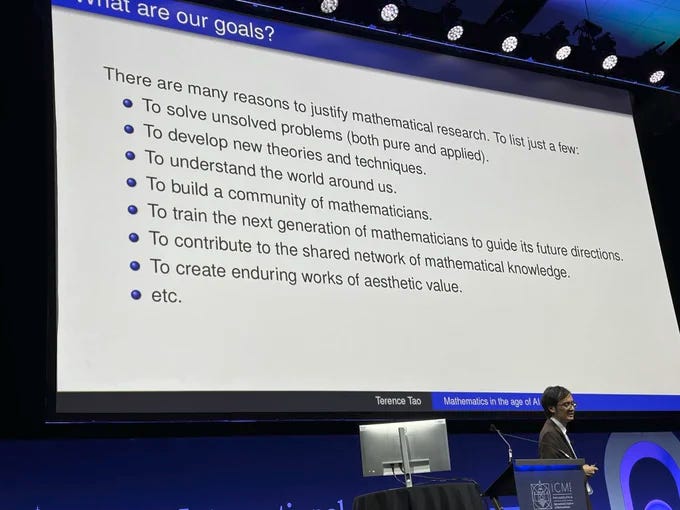 The mathematician Terence Tao stands in front of a presentation slide that says "There are many reasons to justify mathematical research. To list just a few: To solve unsolved problems (both pure and applied). To develop new theories and techniques. To understand the world around us. To build a community of mathematicians. To train the next generation of mathematicians to guide its future directions. To contribute to the shared network of mathematical knowledge. To create enduring works of aesthetic value. etc." The mathematician Terence Tao stands in front of a presentation slide that says "There are many reasons to justify mathematical research. To list just a few: To solve unsolved problems (both pure and applied). To develop new theories and techniques. To understand the world around us. To build a community of mathematicians. To train the next generation of mathematicians to guide its future directions. To contribute to the shared network of mathematical knowledge. To create enduring works of aesthetic value. etc."