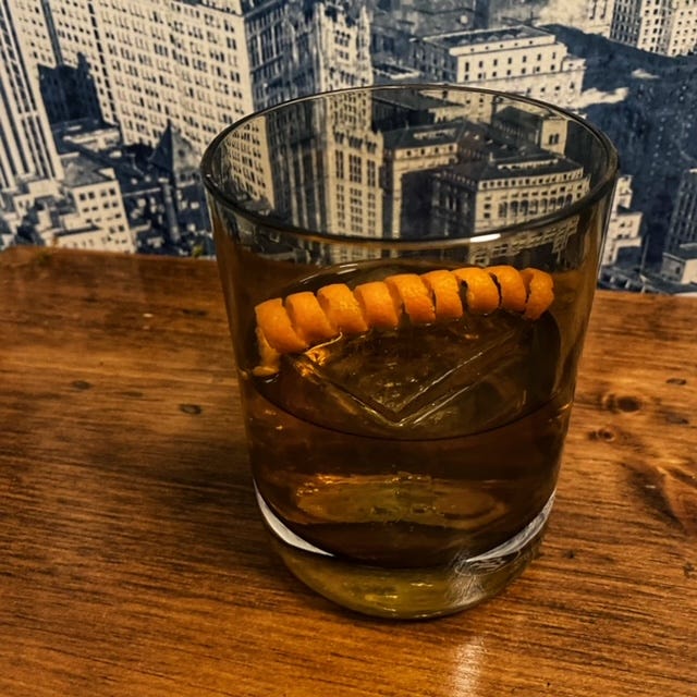 An old fashioned in a lowball glass with a large ice cube and an orange  peel