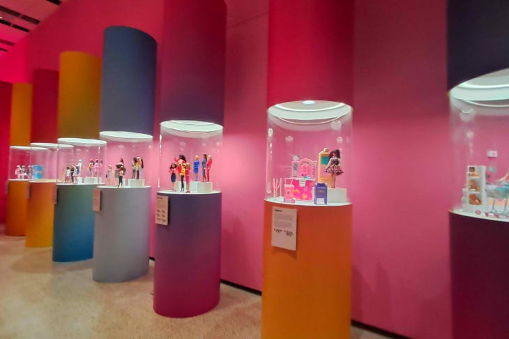 A row of plinths, each topped with a display case containing Barbie dolls