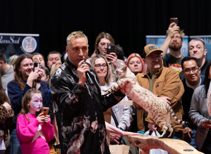 A man with a microphone talking to a crowd while handling a cat