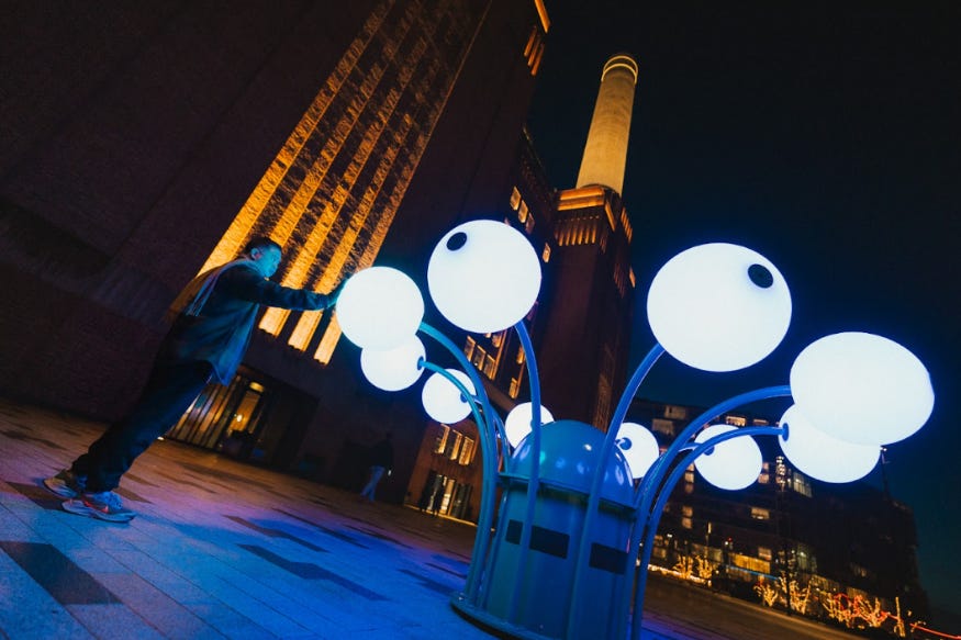 A man reaching out to touch a light art installation in front of Battersea Power Station