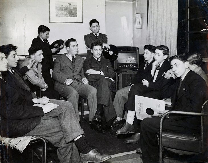 Smartly dressed young men gather around a wireless set - some clutching records