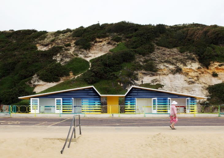 A person walking in front of a striking yellow and blue building at the seaside