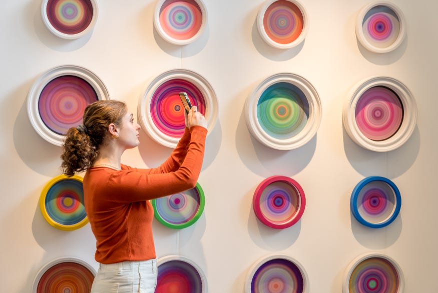 A woman taking a photograph in front of a wall of colourful circular artworks