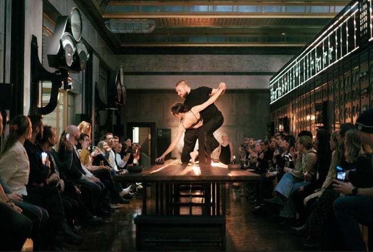 People sitting around a table watching two people dancing on top of it