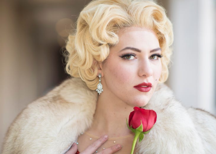 An actress in costume posing as Marilyn Monroe, holding a red rose