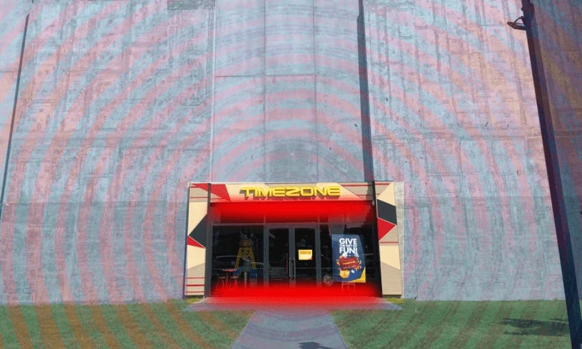 A small technicolour arcade peeks through a giant concrete wall