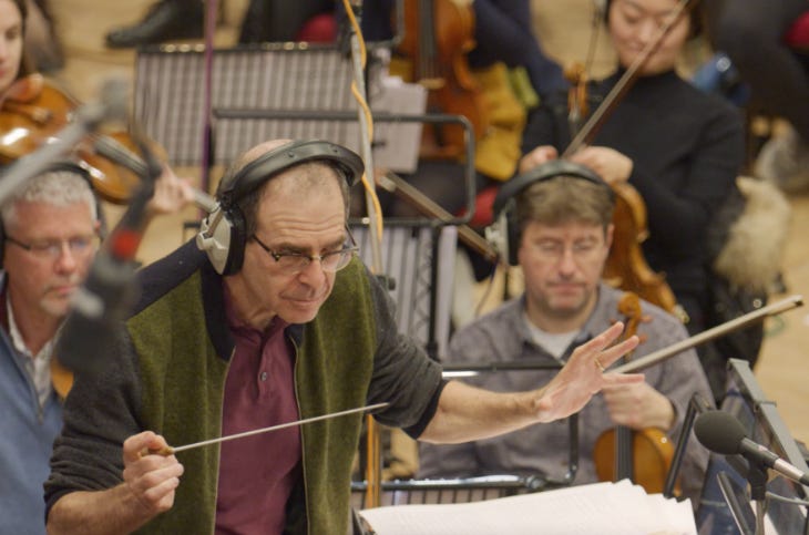 A conductor wearing headphones conducting an orchestra
