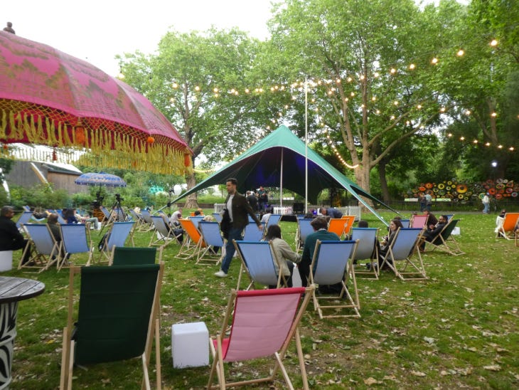 People sitting in deckhairs on a lawn beneath fairylights