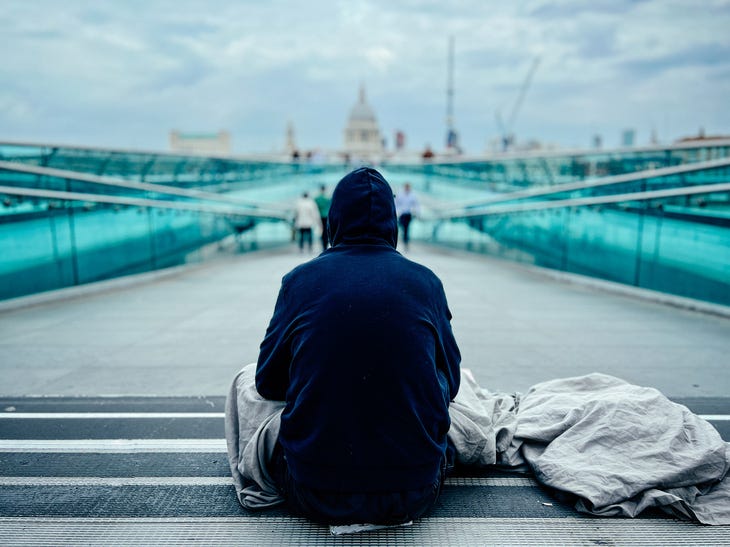 A rough sleeper in a hoodie looking at St Paul's