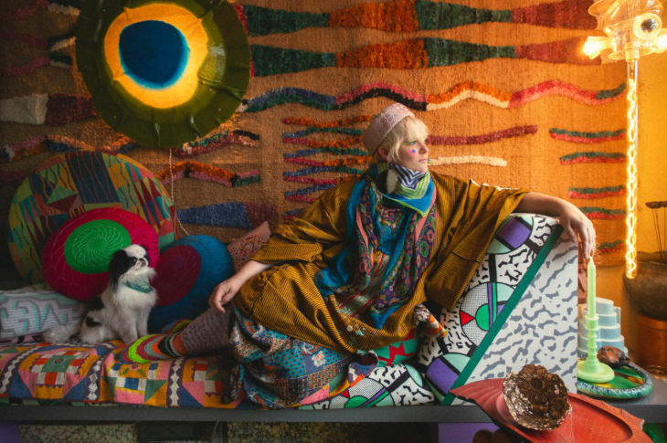 Artist Bethan Laura Wood sitting on a sofa with a dog, surrounded by colourful textiles and decorations