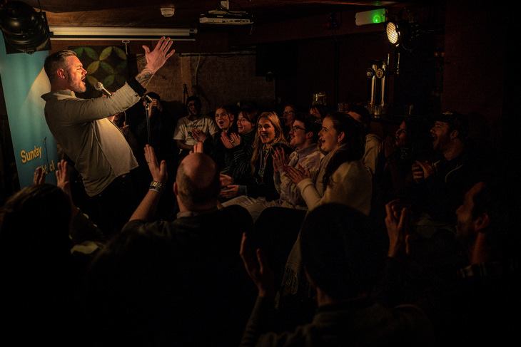 A male comedian entertains a crowd in a dark venue