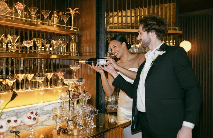 A bride and groom pouring a bottle of champagne