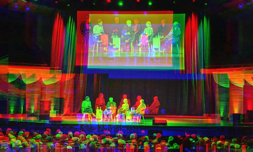 A fuzzy effect on an image of four panellists on stage at the Michael Fowler Centre in Wellington with a big screen behind them