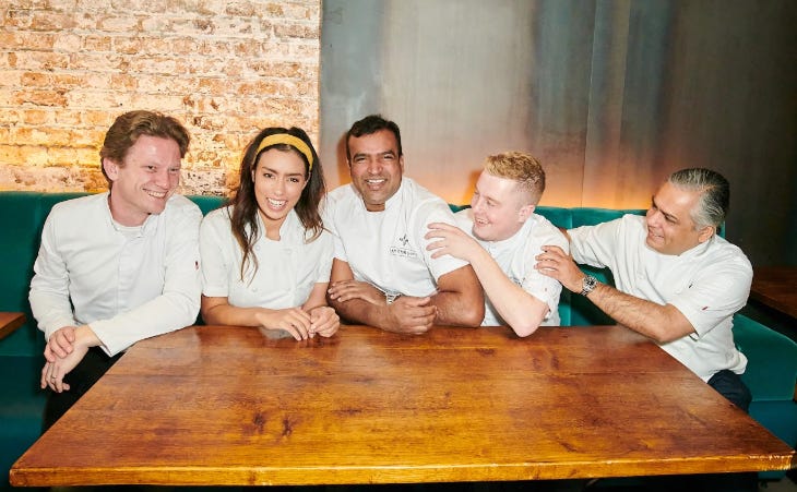 Five chefs sitting around a wooden table