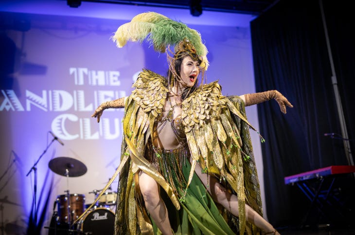 A performer in gold feathered outfit on stage at the Candlelight Club
