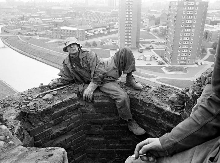 A steeplejack perched on the lip of a tall industrial chimney
