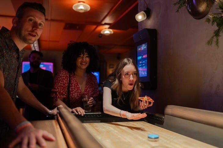 A person playing shuffleboard holding a pizza