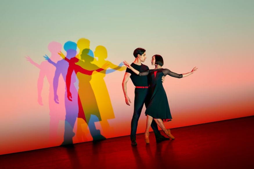 Two people dancing together, silhouetted in duplicate colourfully on the wall behind them