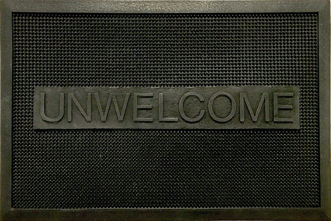 An industrial rubber welcome mat modified so that it reads "unwelcome"